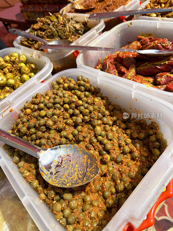 食品市场摊位的特写图像，展示了一排排塑料盒子，里面有泡菜和酸辣酱，金属勺子，填充红辣椒，tenti dela和kerda泡菜，高架视图，重点在前景